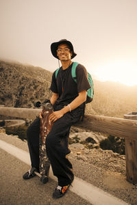 Portrait of smiling young man sitting on wooden guardrail with skateboard