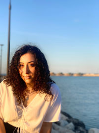 Young woman looking away while standing against sky