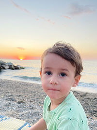 Portrait of boy at beach against sky during sunset
