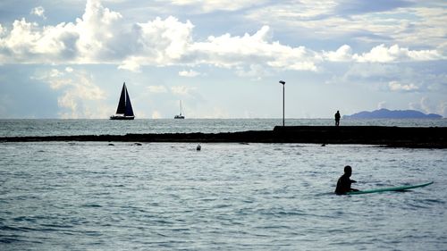 Silhouette people on sailboat in sea against sky