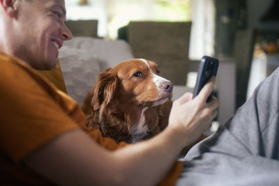 Man sitting on sofa with dog. pet owner taking selfie through mobile phone with his retriever.