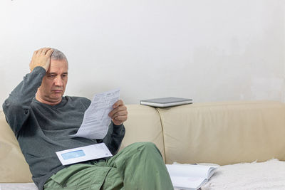 Mature man going through bills, looking worried, reading shocking unexpected news in paper document