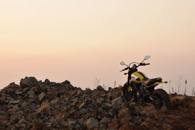 Man riding motorcycle on rock against sky during sunset