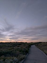 Boardwalk amidst landscape against sky during sunset