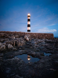 Lighthouse on rock by building against sky