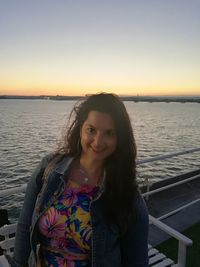 Portrait of smiling woman standing by sea against sky during sunset