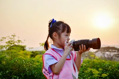 Girl photographing through dslr against sky during sunset