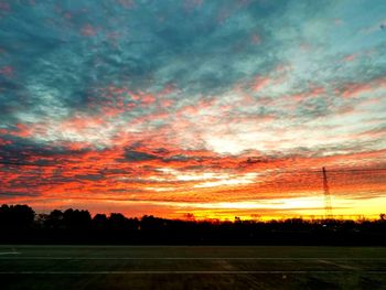 Silhouette trees on field against dramatic sky during sunset