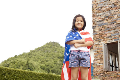 Cute girl with american flag standing against house
