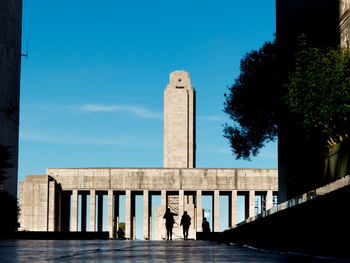 Rear view of people walking by historic building against sky