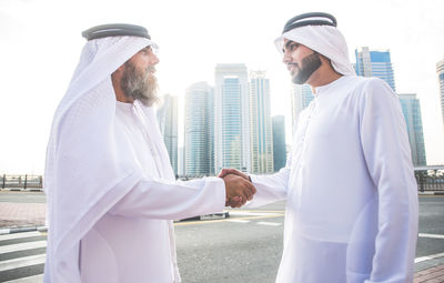 Men wearing dish dash shaking hands on road in city