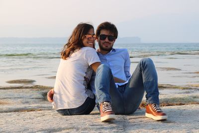 Portrait of loving young couple sitting on rock at beach