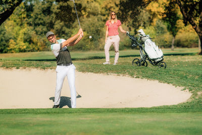 Couple playing golf, golfer coming out of the sand bunker