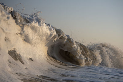Close-up of waves splashing on shore against clear sky