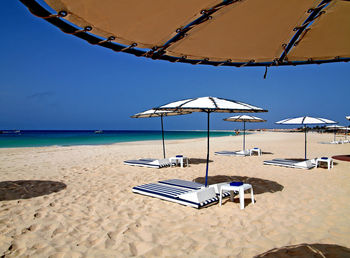 Deck chairs on beach against sky