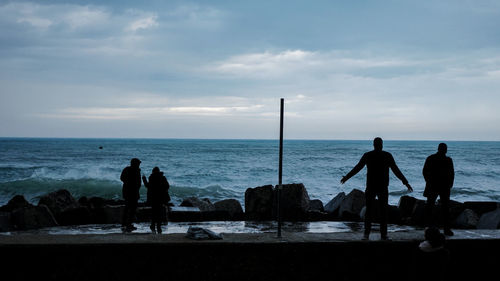 Silhouette people at beach against sky