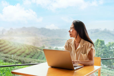 Young woman using laptop while sitting on field