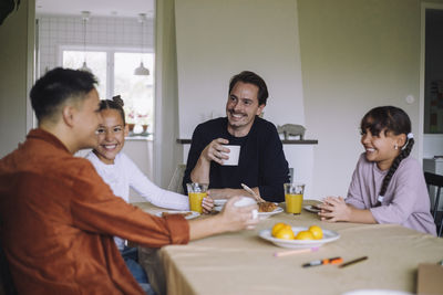 Happy gay couple spending leisure time with daughters while having breakfast at dining table in home