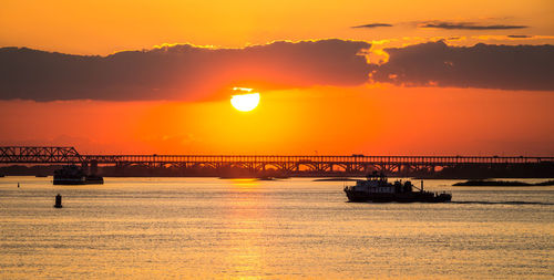 Silhouette bridge over sea against orange sky