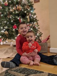 Full length of cute girl sitting on christmas tree