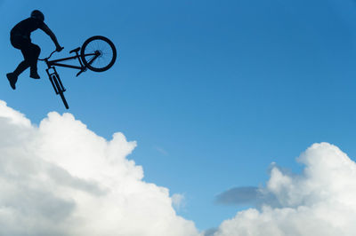 Low angle view of silhouette man doing stunt with bicycle against blue sky