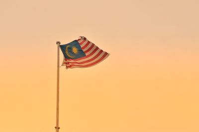 Low angle view of flag against orange sky