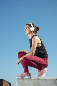 Woman wearing headphones and listening to music outside in the sun, urban setting.