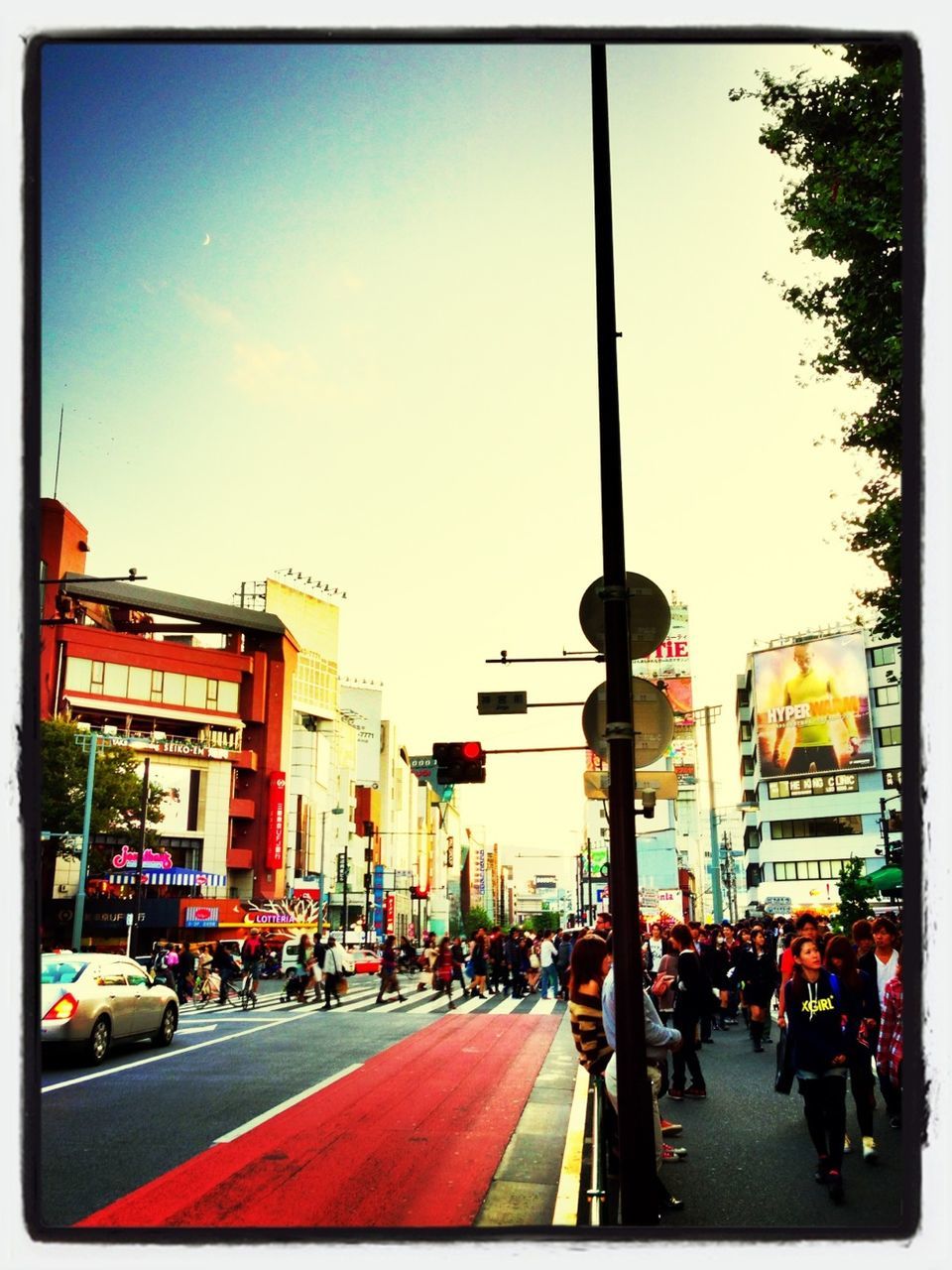 street, transfer print, transportation, city, building exterior, car, architecture, land vehicle, city life, built structure, city street, road, mode of transport, auto post production filter, incidental people, sky, large group of people, traffic, person