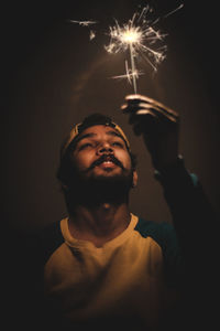 Portrait of young man holding sparkler at night