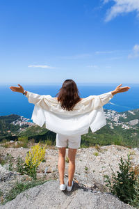 Young beautiful woman stands with her back and looks at the old town of budva, montenegro.