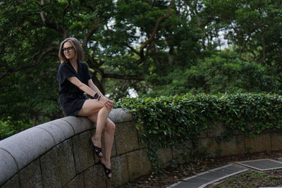 Full length of young woman sitting on retaining wall
