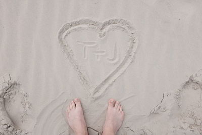 Low section of person standing by heart shape on sandy beach