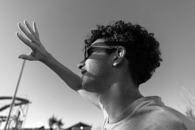 Young latin guy looking at the sun and covering his hand causing shadows on his face.