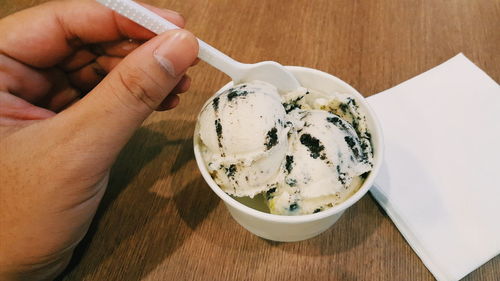 Cropped hand of person holding ice cream spoon on table