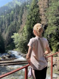 Rear view of woman standing by railing against trees