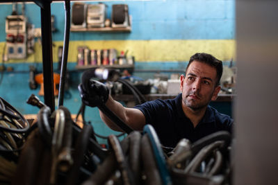 Professional adult male mechanic taking hose for painting car from storage while working in repair service workshop