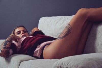 Portrait of seductive tattooed woman relaxing on sofa at home