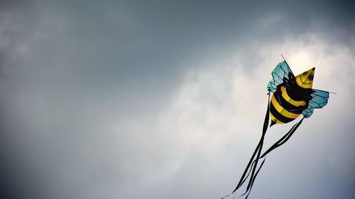 Low angle view of kite flying against cloudy sky