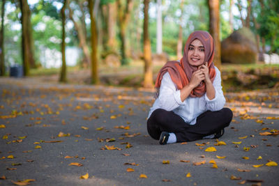 Portrait of smiling woman sitting amidst autumn leaves on road during autumn