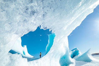 Unrecognizable traveler hiker admiring spectacular scenery of frozen seashore with ice and snow in winter in iceland