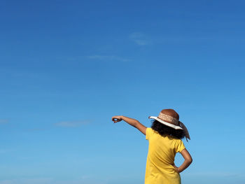 Rear view of girl pointing standing against blue sky