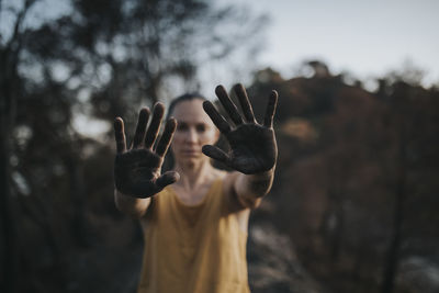 Woman showing hands black with ash standing in burnt forest