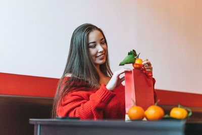 Beautiful asian woman in red clothes with gift bag with mandarins in cafe, chinese new year