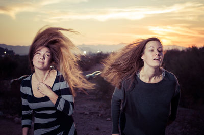 Beautiful women with tousled hair on field against sky during sunset