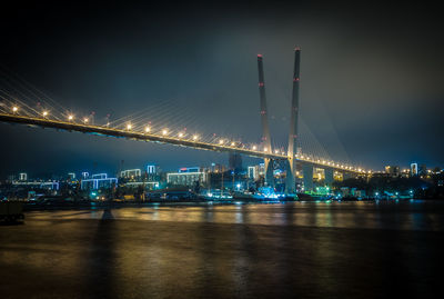 Illuminated factory by river against sky at night