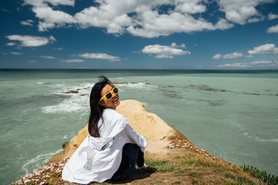 Woman sitting on shore at beach against sky