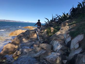 Man standing on rock by sea against clear sky