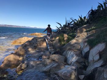 Rear view of boy walking on rocks at beach