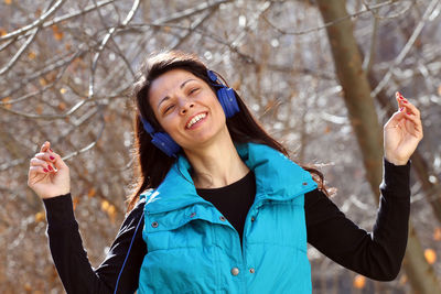 Portrait of smiling woman wearing headphones against tree