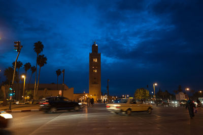 Cars on road by illuminated buildings against sky at night